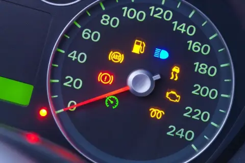 Cruscotto auto con spie accese: serbatoio, ABS, luci blu, controllo stabilità, motore e altre. L'ago del tachimetro indica una velocità bassa.