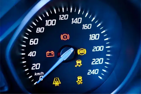 Cruscotto auto con tachimetro e spie accese: spia punto esclamativo giallo, ABS, controllo stabilità e batteria.