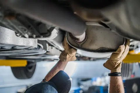 Mani guantate lavorano sul sistema di scarico di un'auto, forse per sostituire il catalizzatore auto.