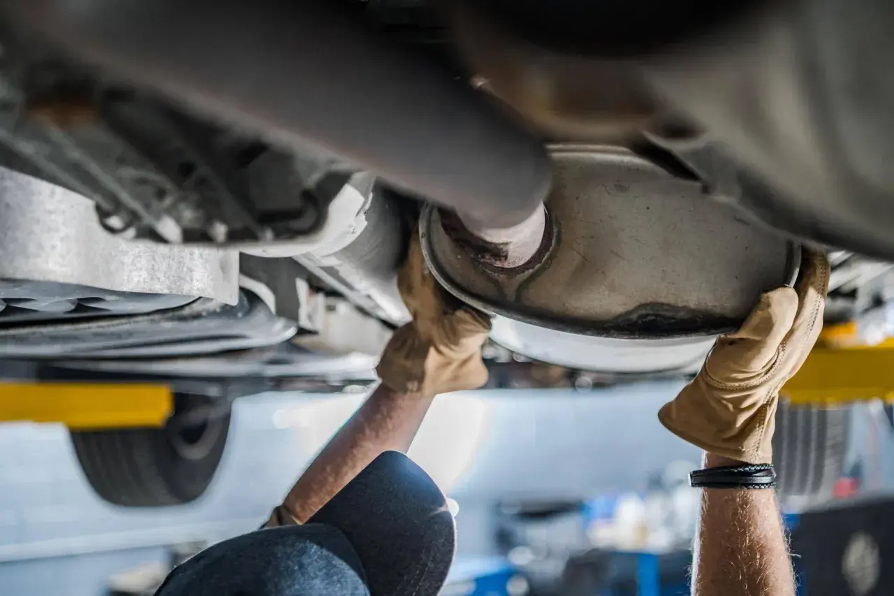 Mani guantate lavorano sul sistema di scarico di un'auto, forse per sostituire il catalizzatore auto.